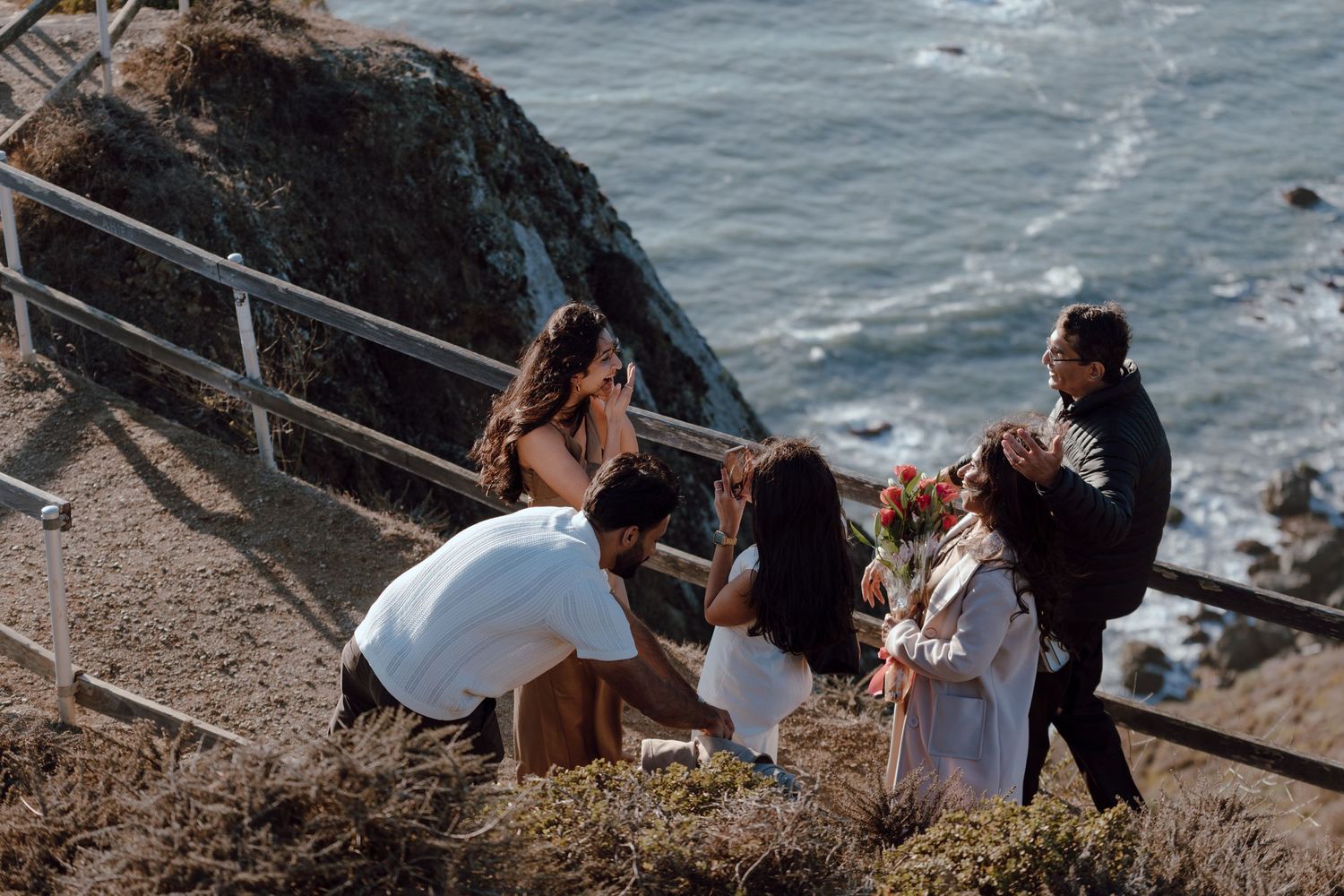 Small group gathers on cliffside overlook near ocean for intimate celebration.
