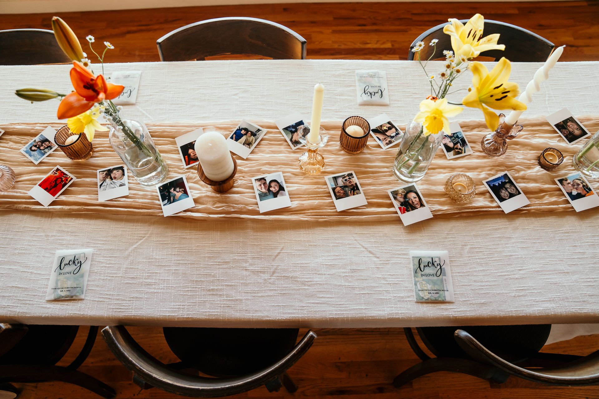 Elegant wedding reception table with polaroid photos, yellow lily centerpieces, and candles on a rustic wooden table.