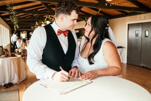 Bride and groom signing marriage certificate at a decorated indoor wedding reception.
