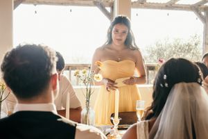 Bridesmaid in yellow dress delivering a heartfelt speech at a sunlit wedding reception.