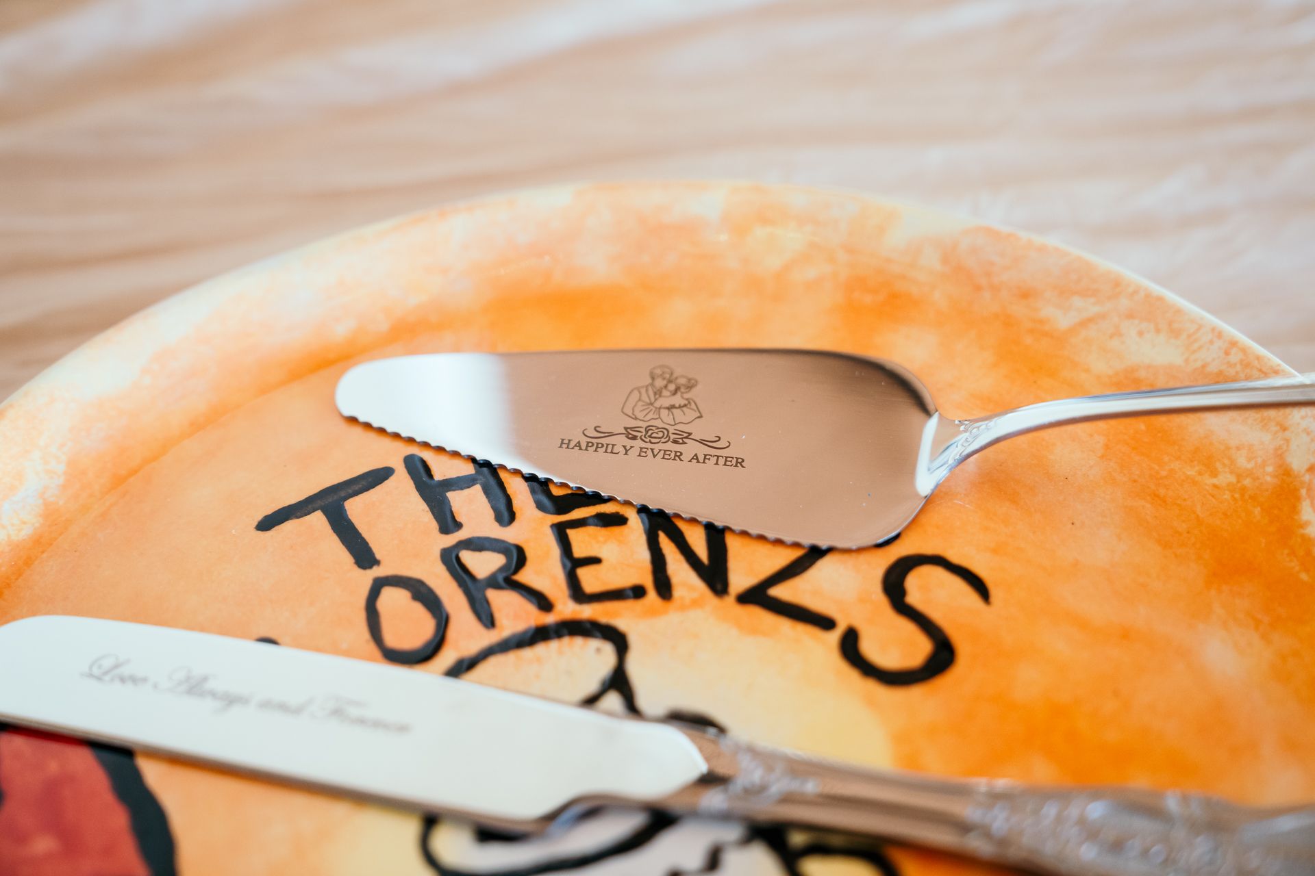 A cheese spreader resting on a decorated cheesecake with 'The Lorenzs' written in chocolate sauce.