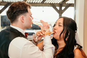 Newlywed couple shares a champagne toast drinking from elegant flutes at their wedding reception.