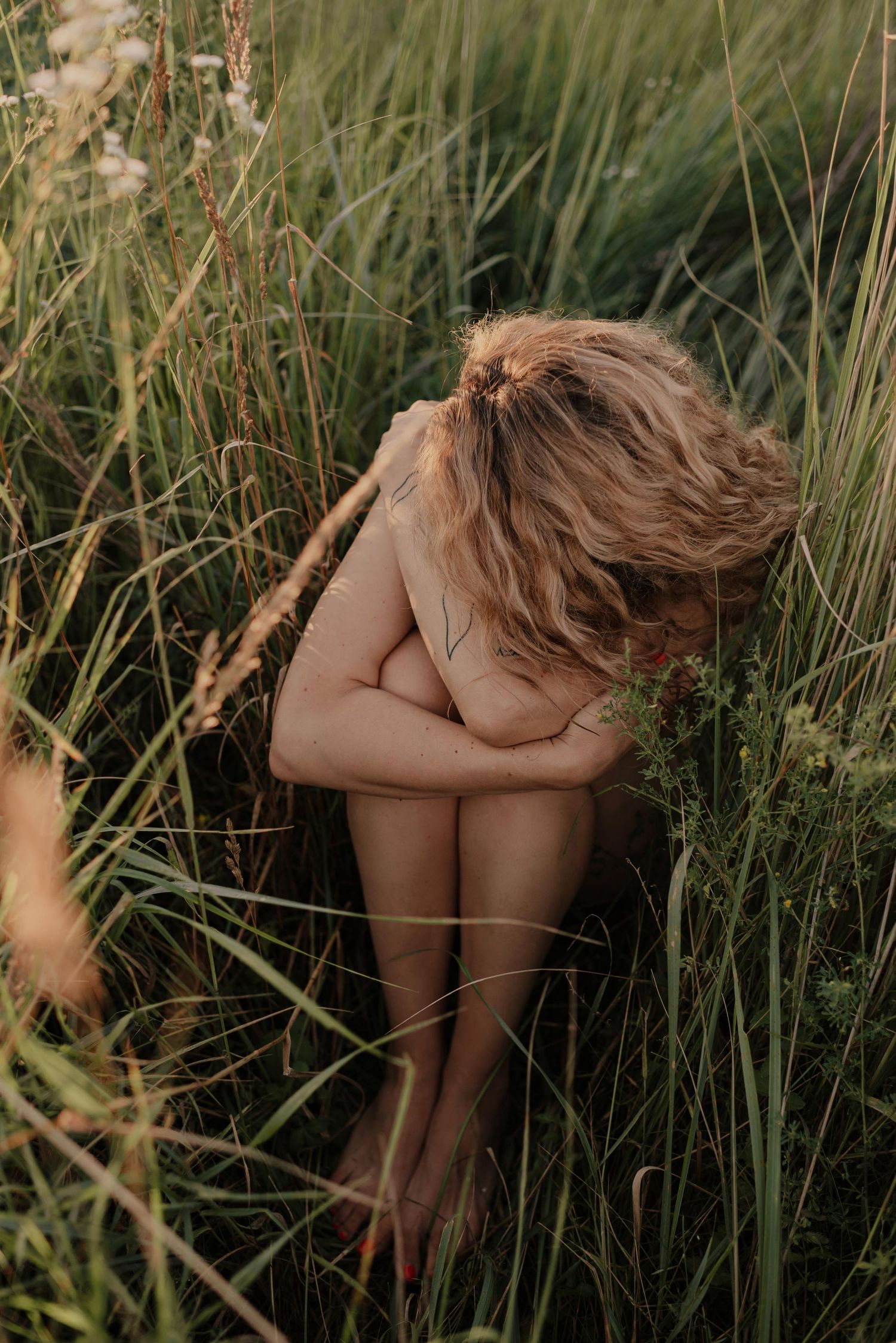 Artistic portrait series showing a figure crouching among tall green grass in natural sunlight.