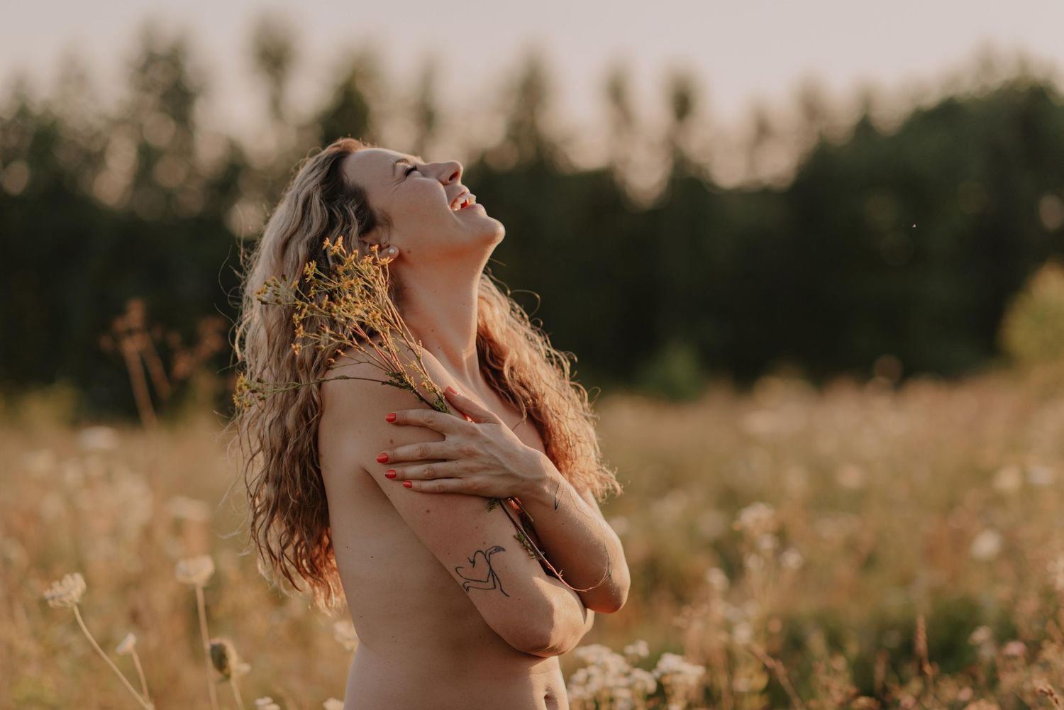 A figure stands in a sunlit golden field at sunset with eyes closed and arms crossed in peaceful contemplation.