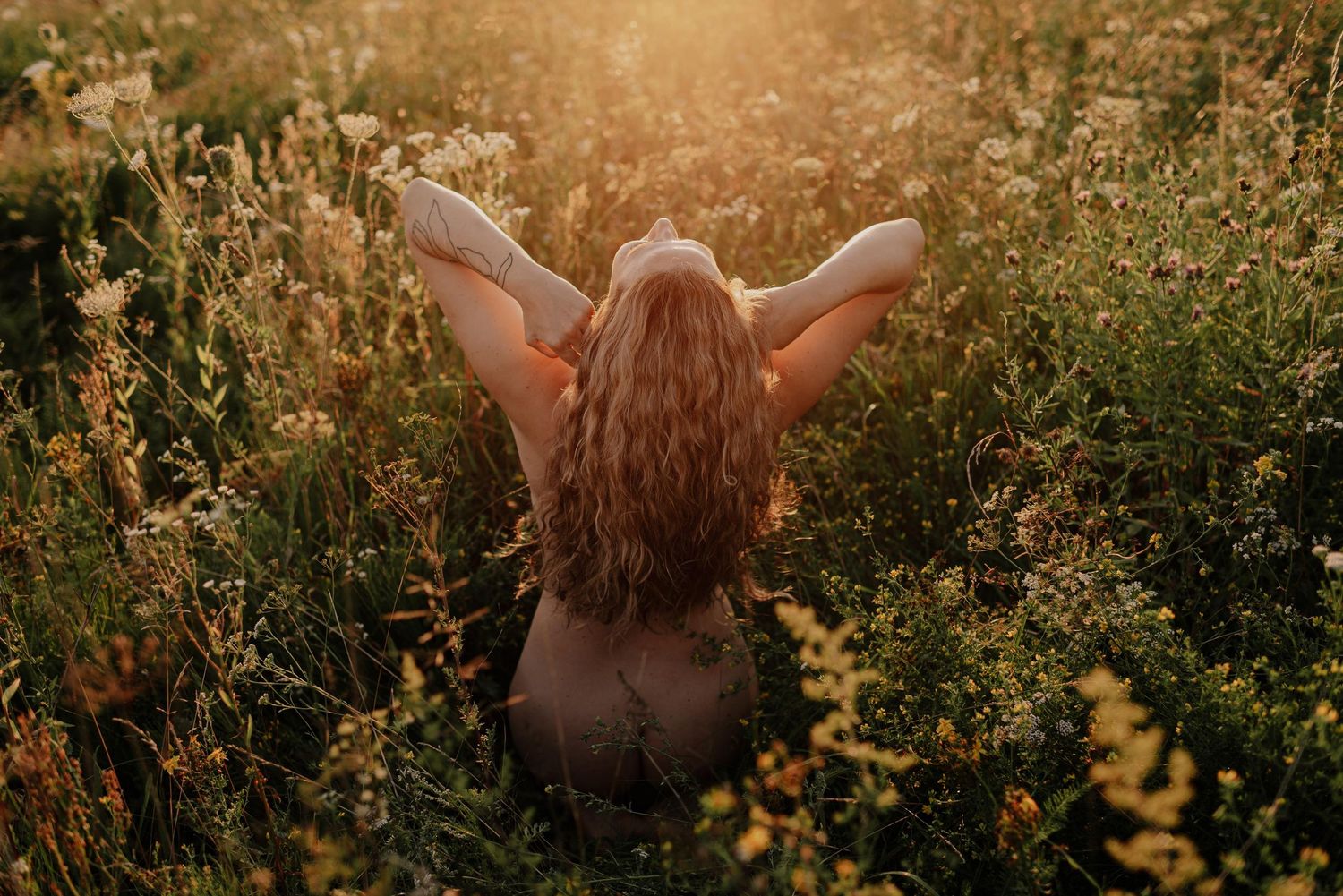 Person with long flowing hair dances joyfully in a sunlit meadow surrounded by wildflowers at golden hour.