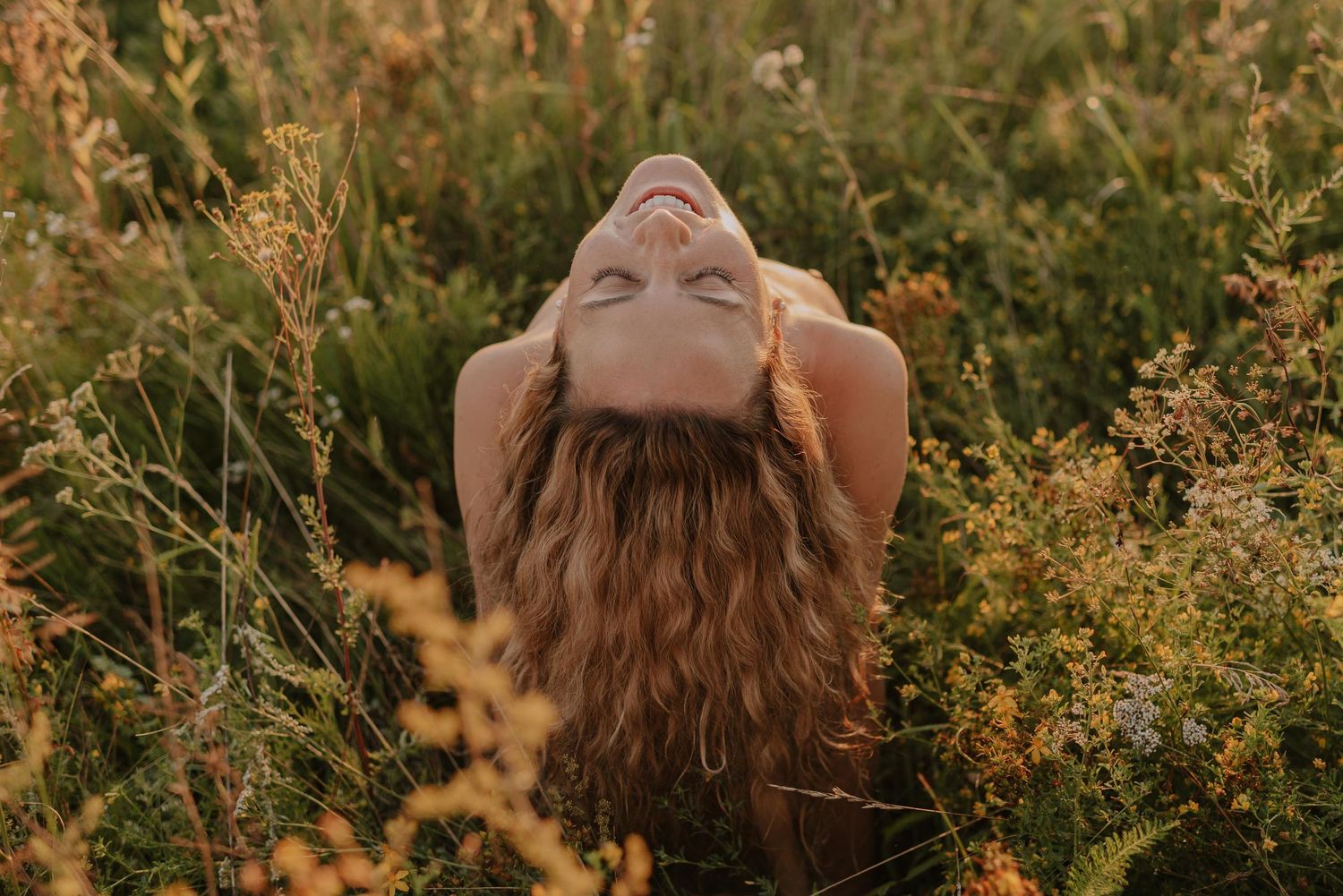 Long-haired figure photographed from above in a golden field of wildflowers at sunset.
