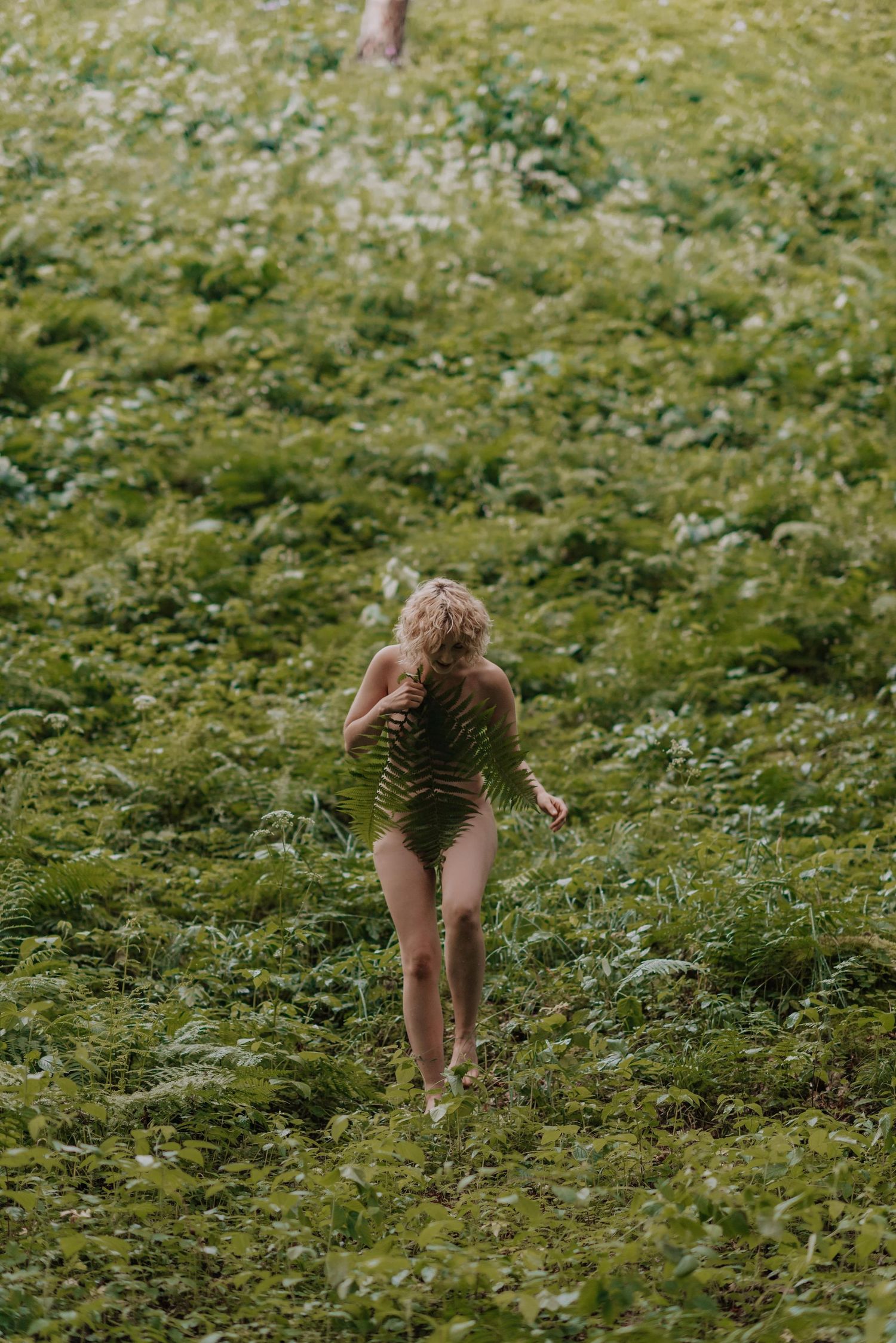 Someone walking barefoot through a field of green plants and white flowers in the sunlight.