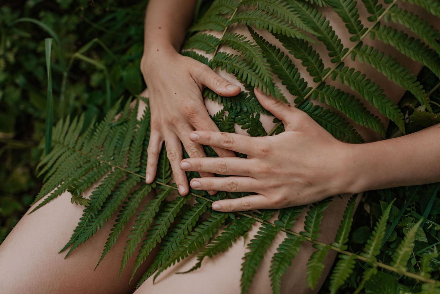 Gentle hands emerging from behind delicate fern fronds in a forest setting.