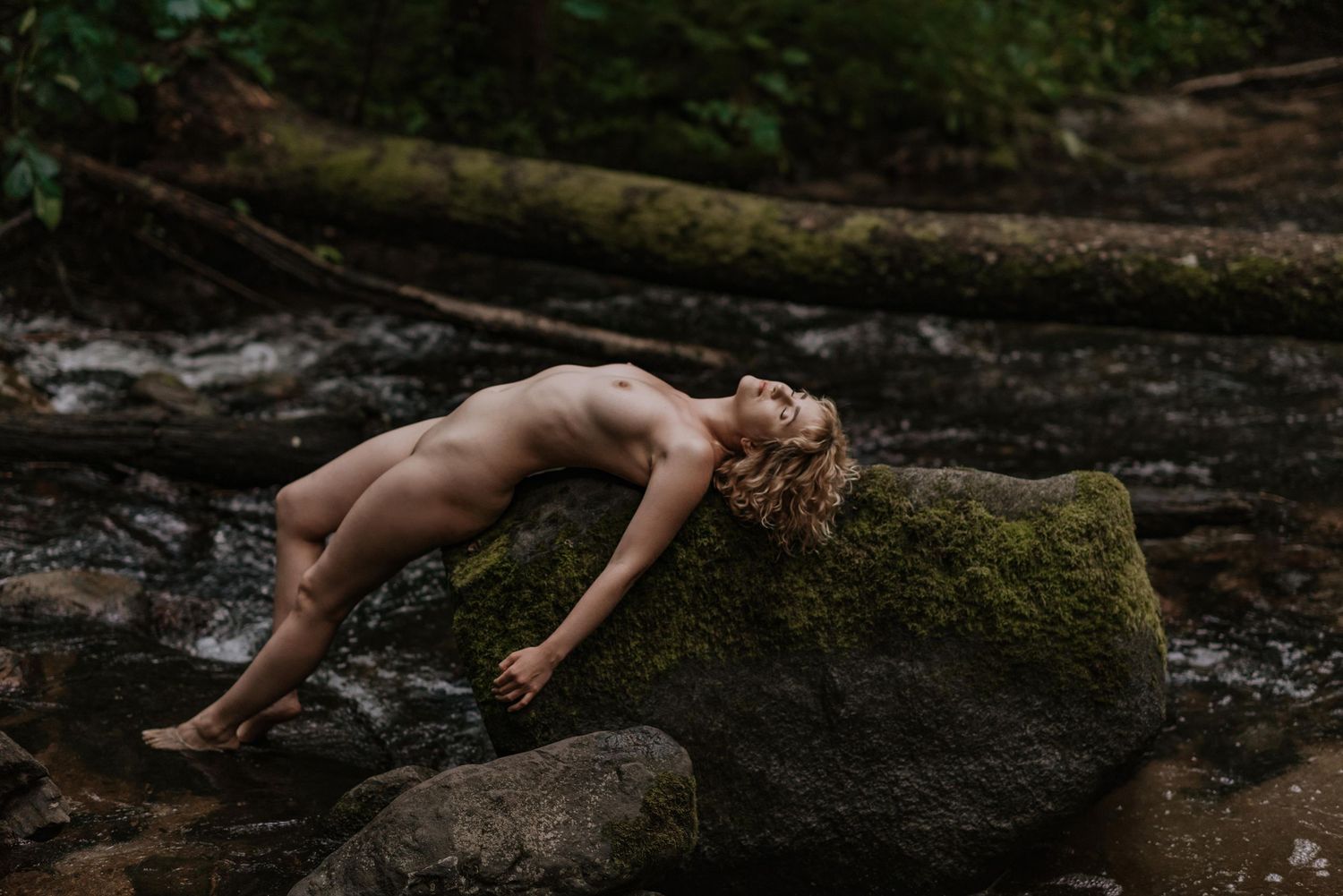 Hand reaching out to touch moss-covered rocks in a dark forest setting with dramatic lighting.