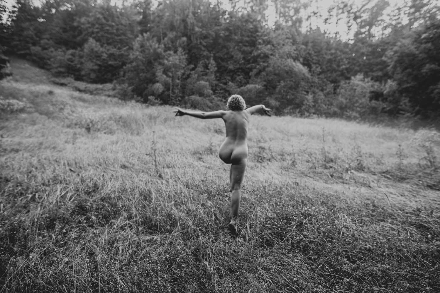 A black and white photography sequence of small figures walking through tall grass on a winding hillside path.