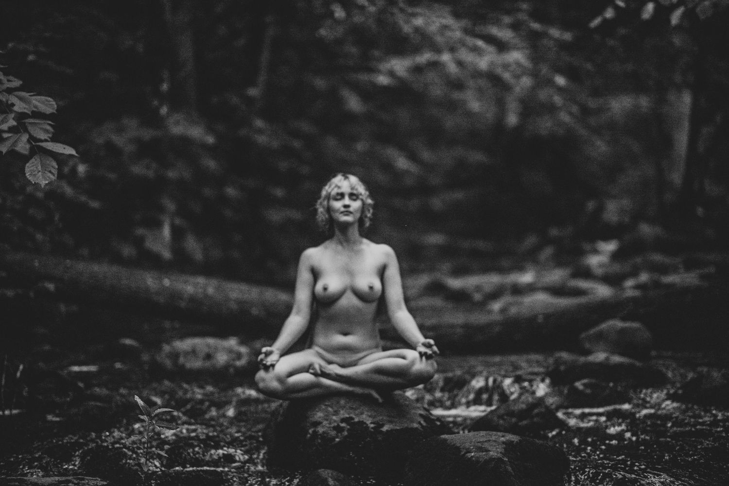 Forest nymph lounges on wet stones in a dark mossy stream in ethereal black and white photography.