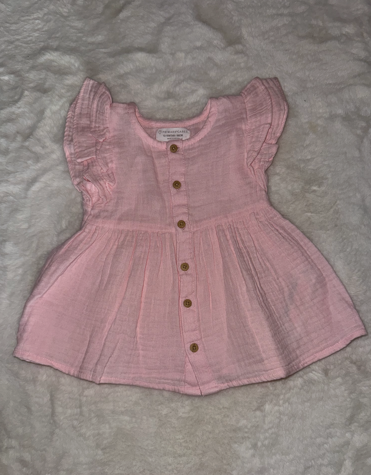 Pink cotton baby dress top with ruffled sleeves and button details shown from different angles.