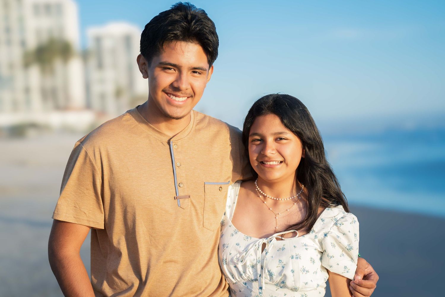 A happy family poses together on the beach at sunset in coordinating blue and beige outfits.