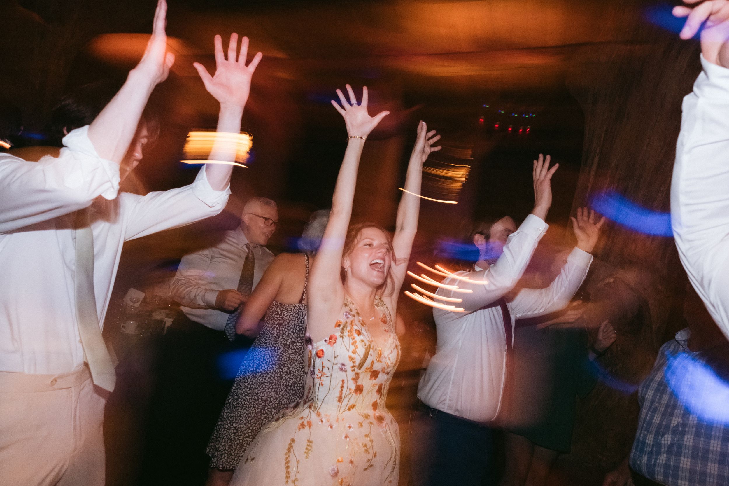 Party guests dancing energetically on a dance floor with raised arms in motion blur at a wedding celebration.