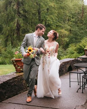 A happy couple laughs together at an outdoor wedding venue with sunflowers and greenery in the background.