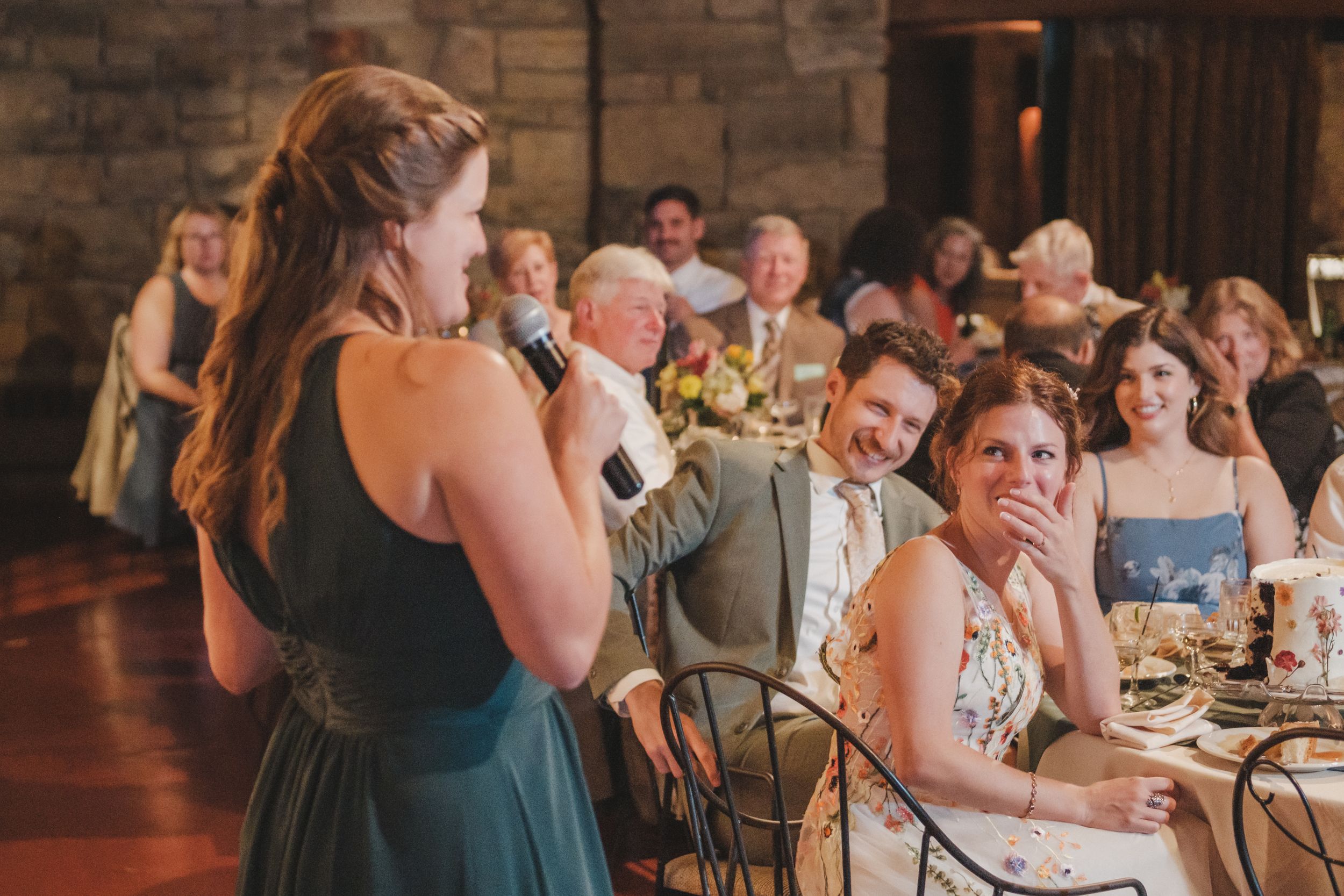 Guests react with laughter and joy during a candid moment at a wedding reception in a rustic venue.