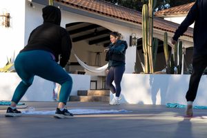 People exercising during an outdoor fitness class at a house patio with Spanish-style architecture and a cactus.