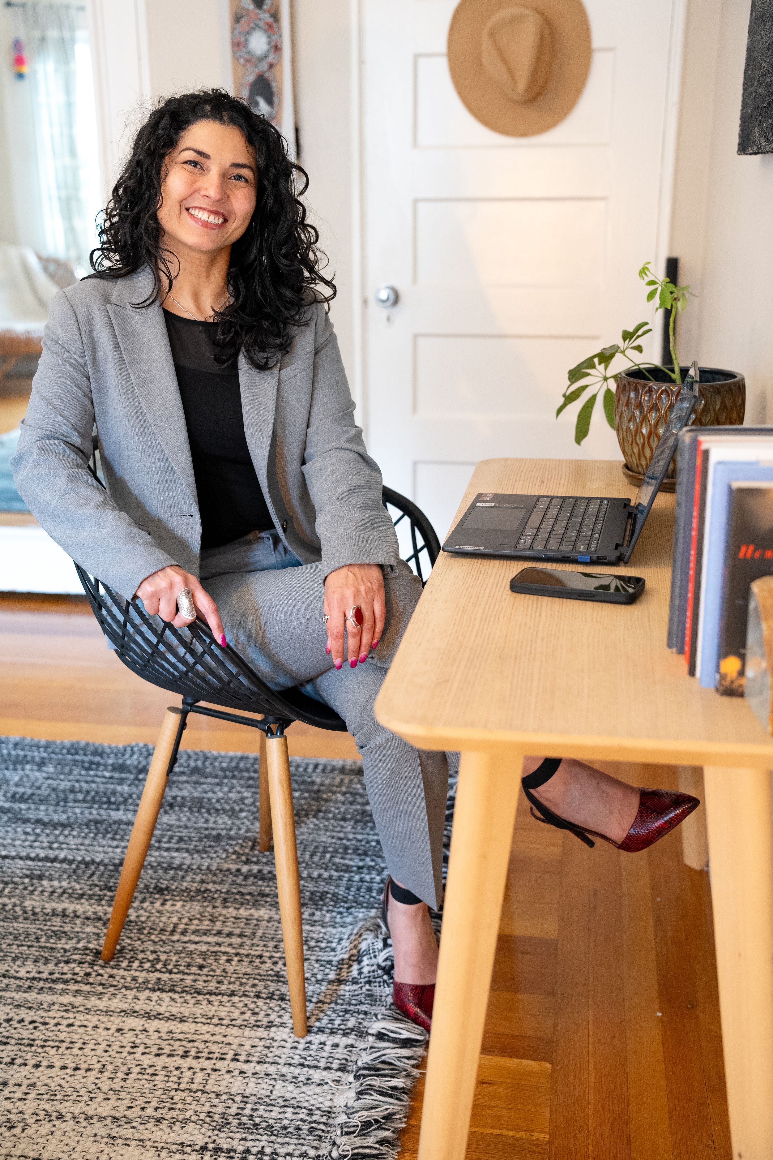 Professional working from home sits at wooden desk with laptop in modern home office with gray rug and tan decor.