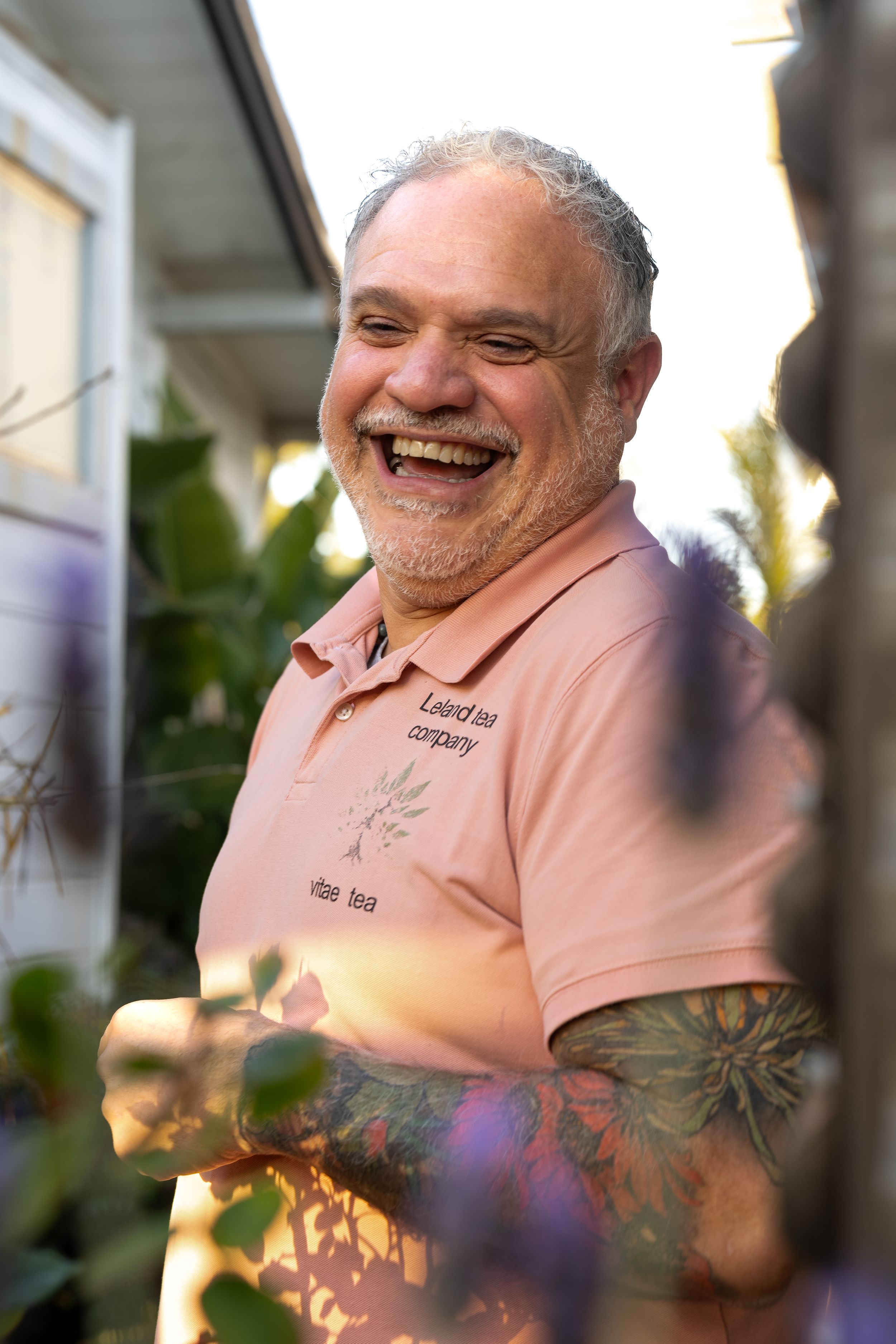 Person in pink polo shirt smiling outdoors with lens flares and foliage in the background.