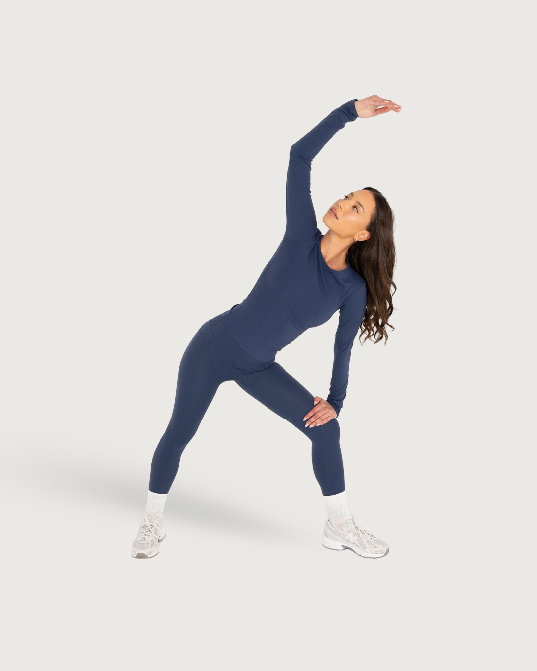 Woman demonstrates yoga stretches in navy blue athletic wear and white sneakers on light background.