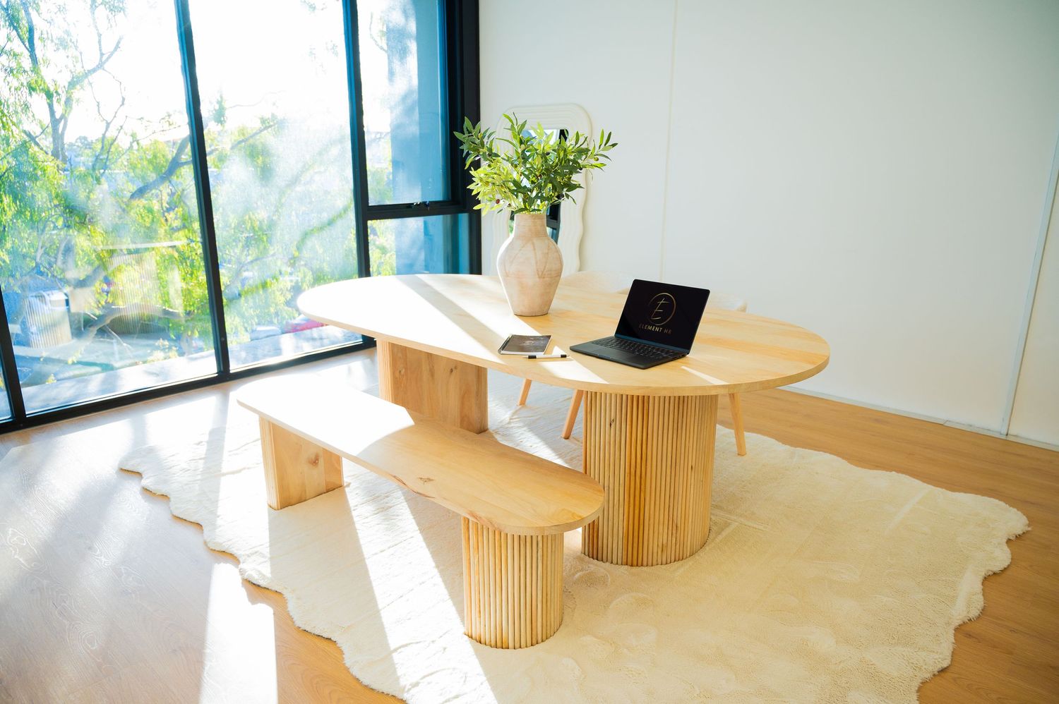 Modern wooden meditation stool sits in a bright sunlit room with white walls and large windows.