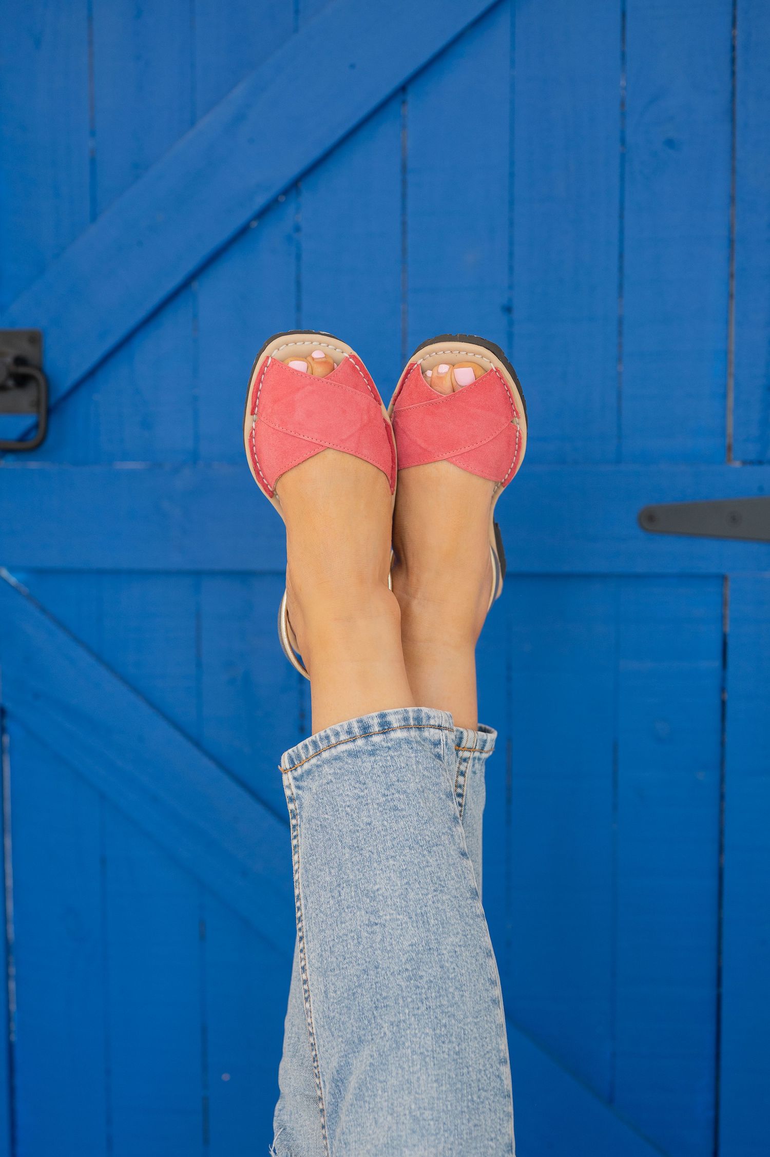 Feet wearing coral pink ballet flats propped up against a bright blue wooden door or wall.