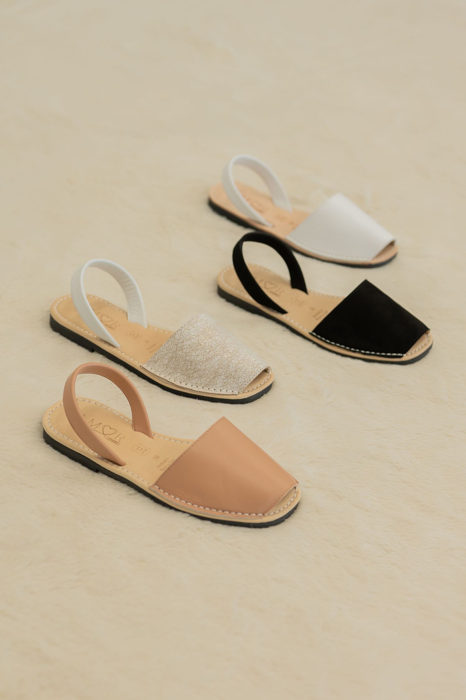 Stylish leather Menorcan sandals in tan, black, and white colors arranged in a minimalist composition on beige background.