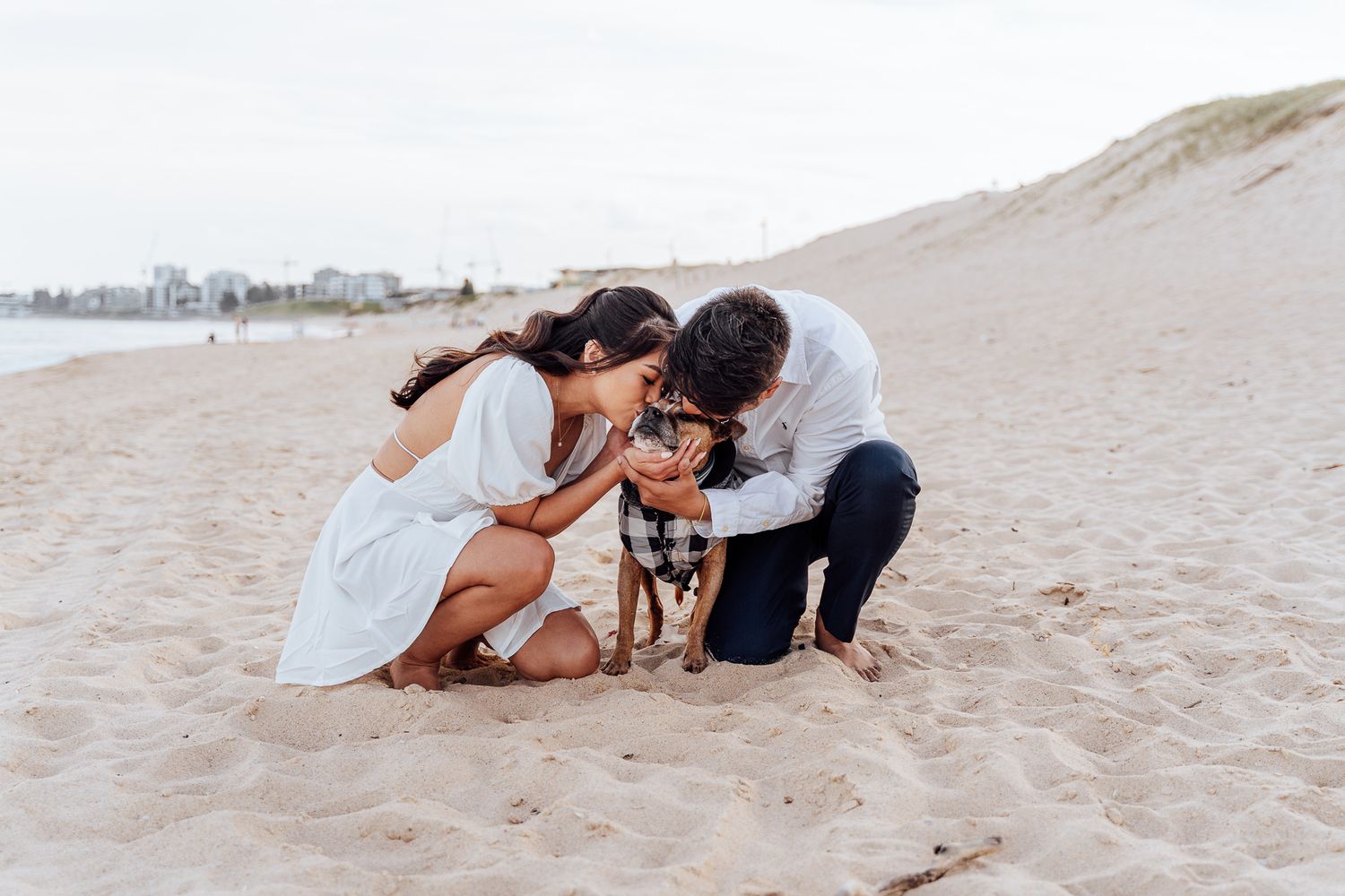 Romantic couple embraces and shares intimate moments together on a sandy beach at sunset.