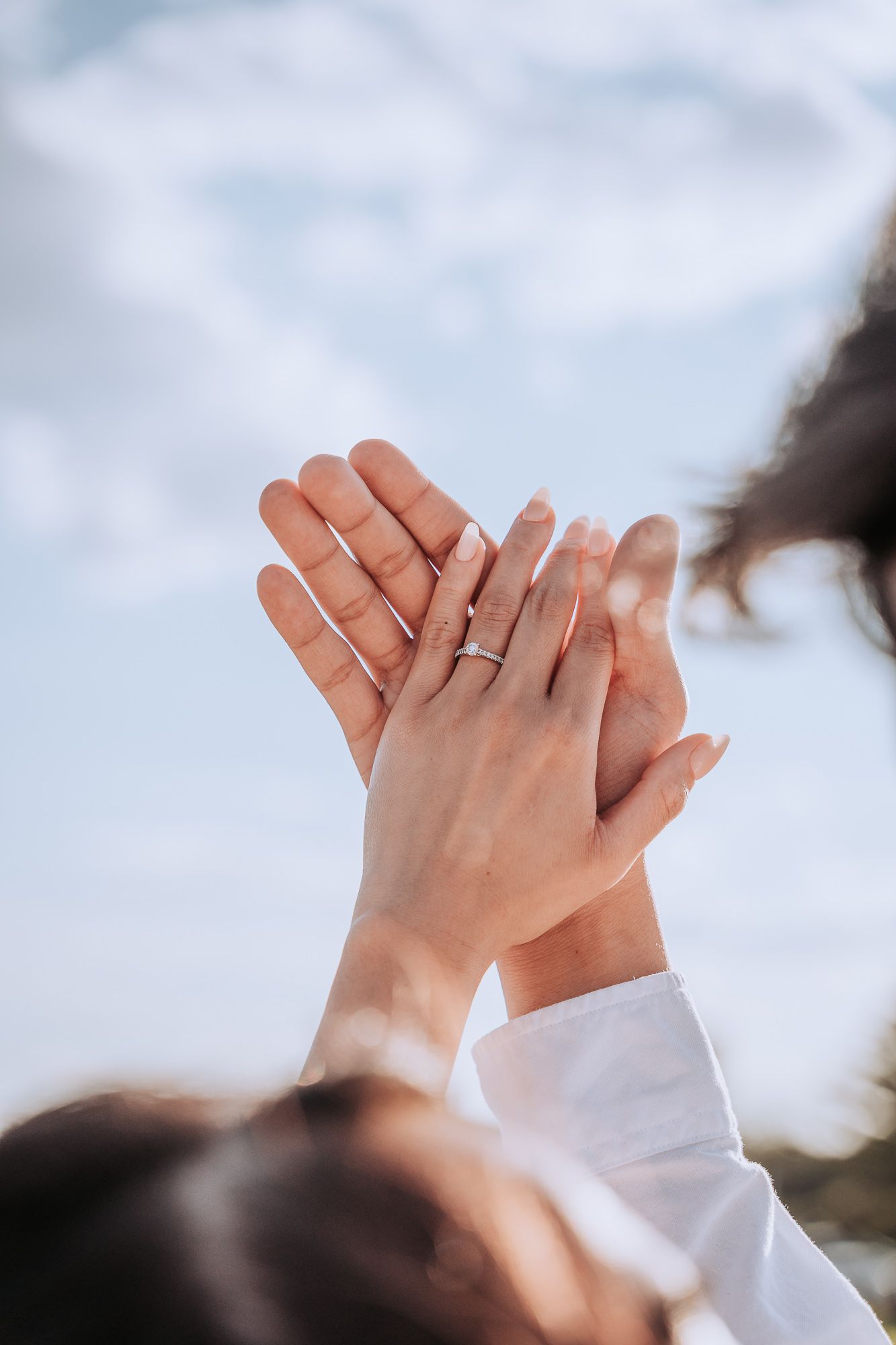 Two hands reach up against a cloudy sky background in an intimate gesture.