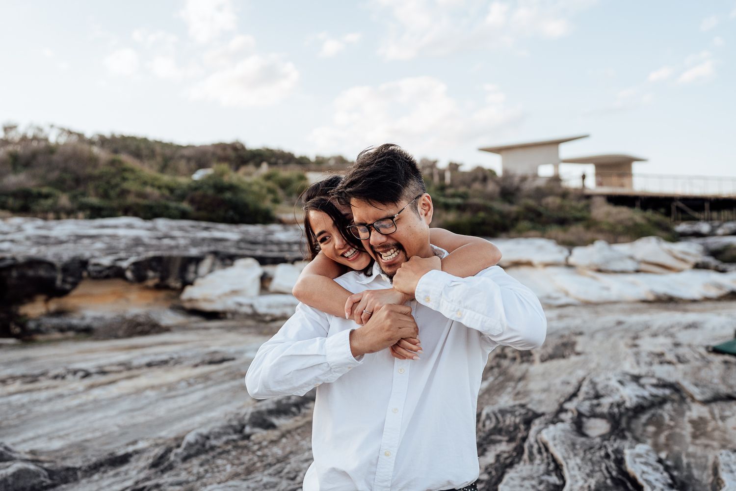 A tender moment captured between two people on rocky coastal terrain.