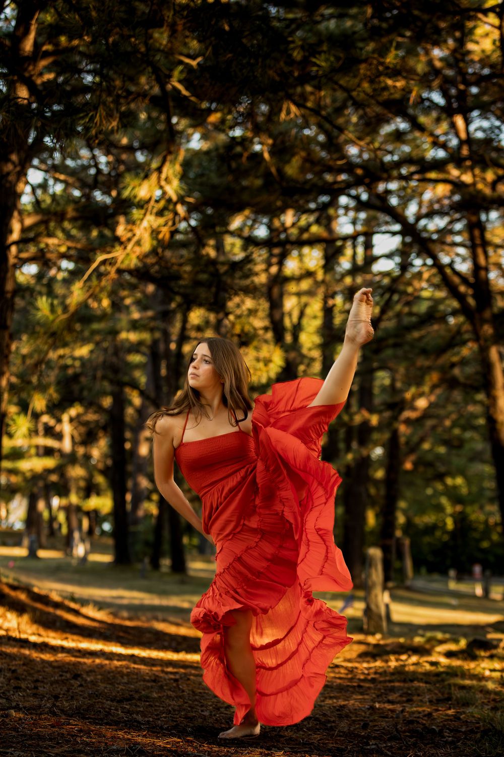 A figure in a flowing red dress dances gracefully through a sunlit forest during golden hour.
