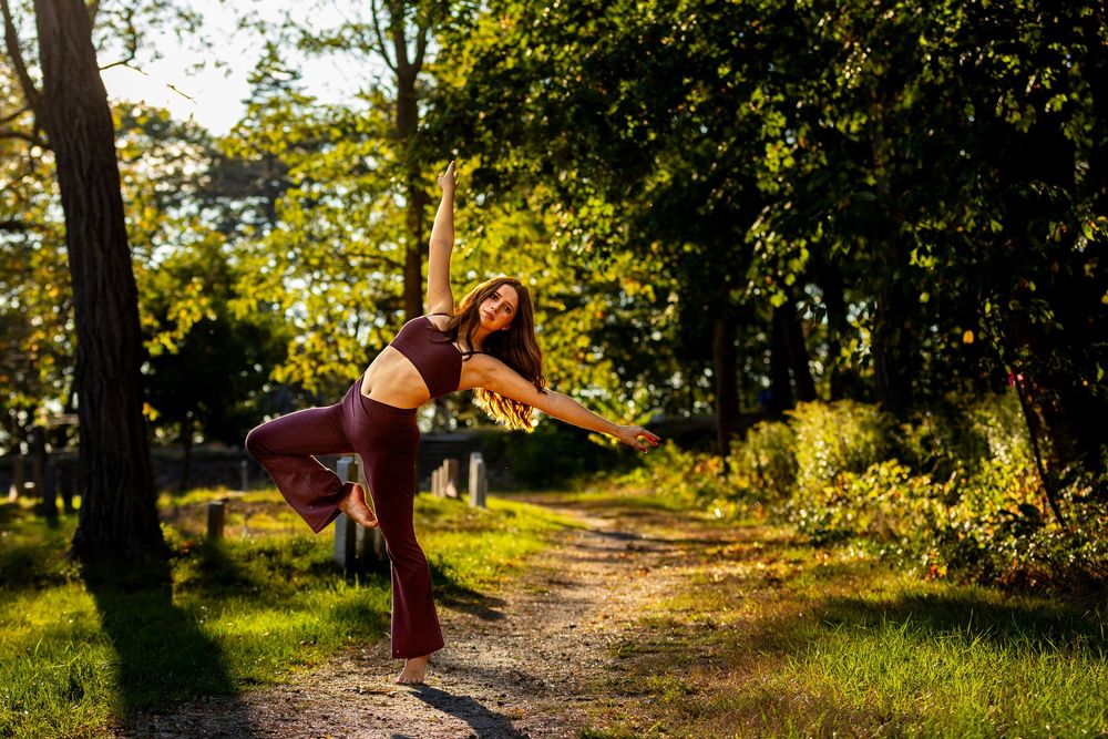 A figure in a red dress twirls gracefully along a sunlit forest path during golden hour.