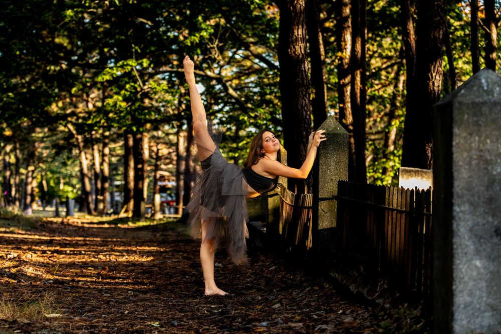 A figure dances gracefully between trees in a sunlit forest, creating an artistic silhouette against natural scenery.