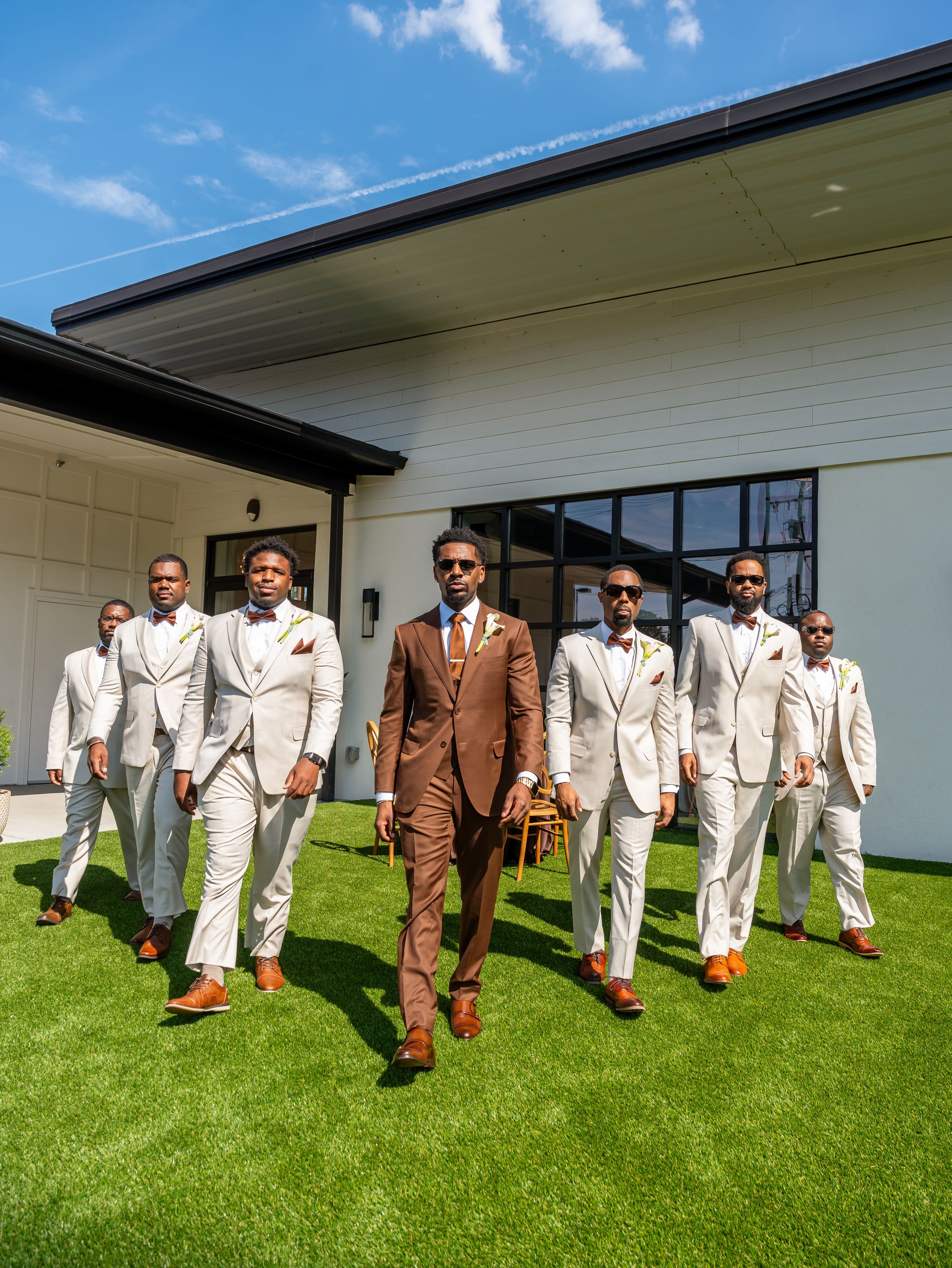 Photographer captues Wedding party in cream and brown suits walking together on grass in North Carolina