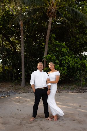 Romantic beach photoshoot with couple sitting on sandy shore surrounded by palm trees.