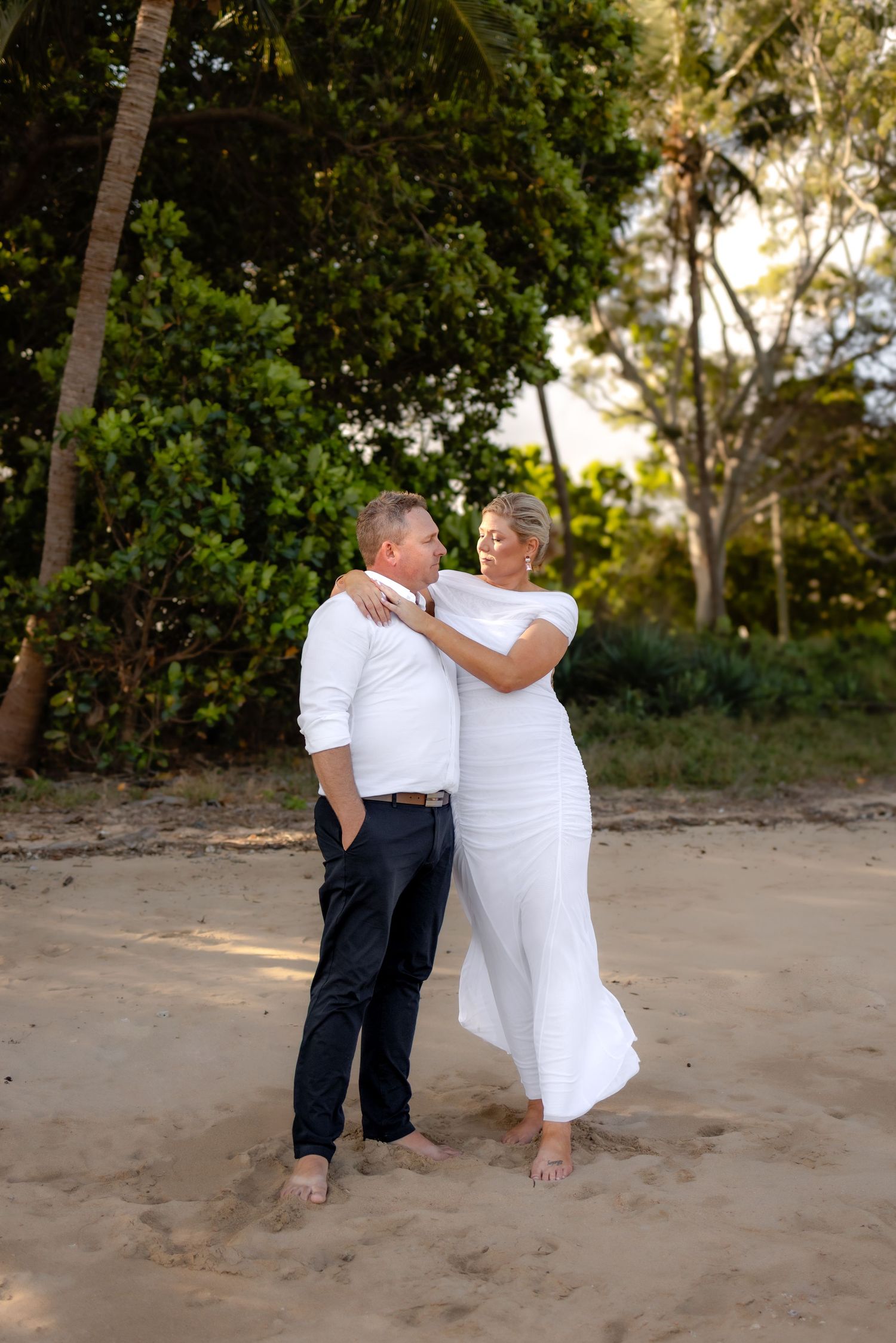 Couple in white clothing sharing romantic moments on sandy beach.