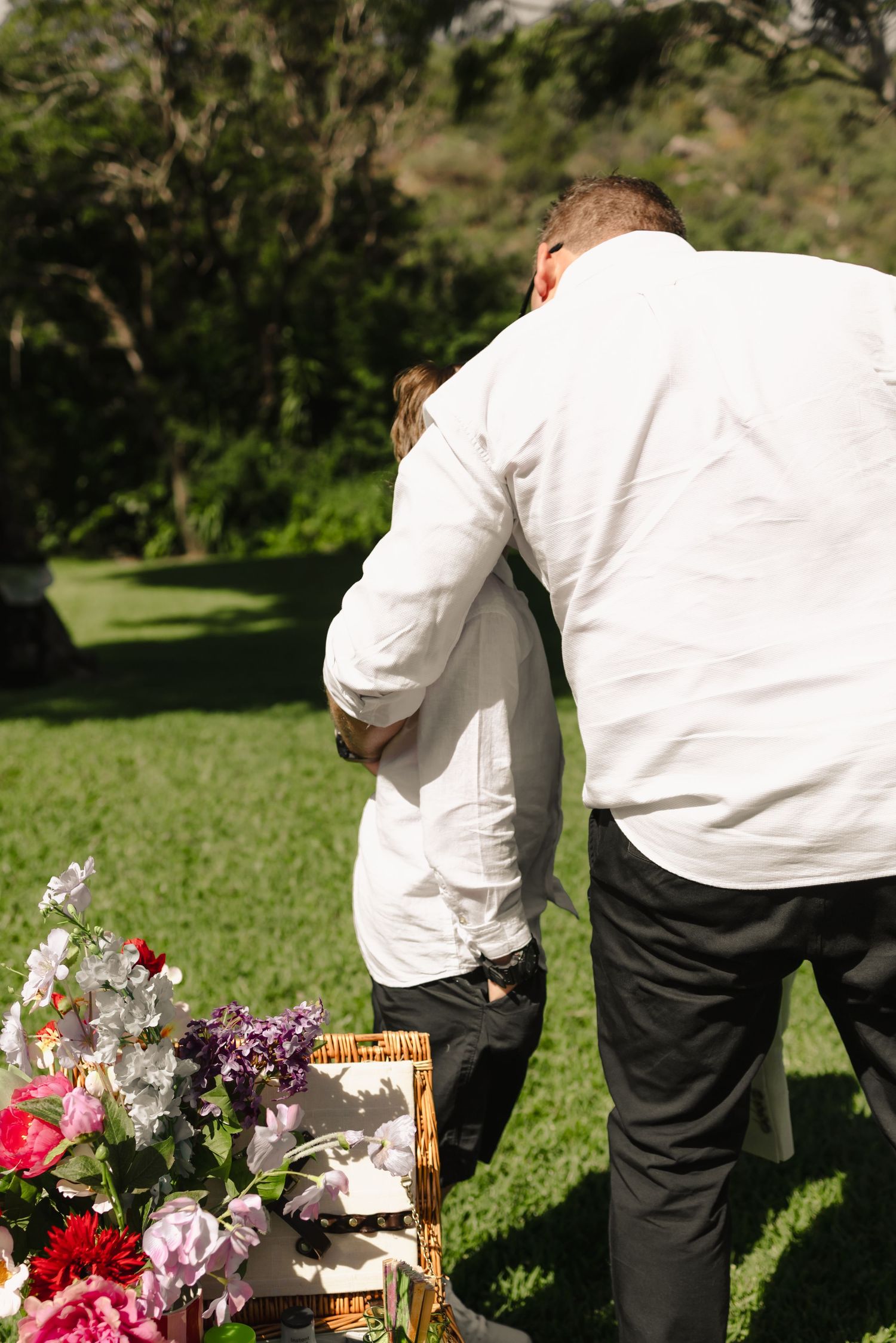 Wedding guests gathered around decorative outdoor displays with colorful flowers and wooden accents.
