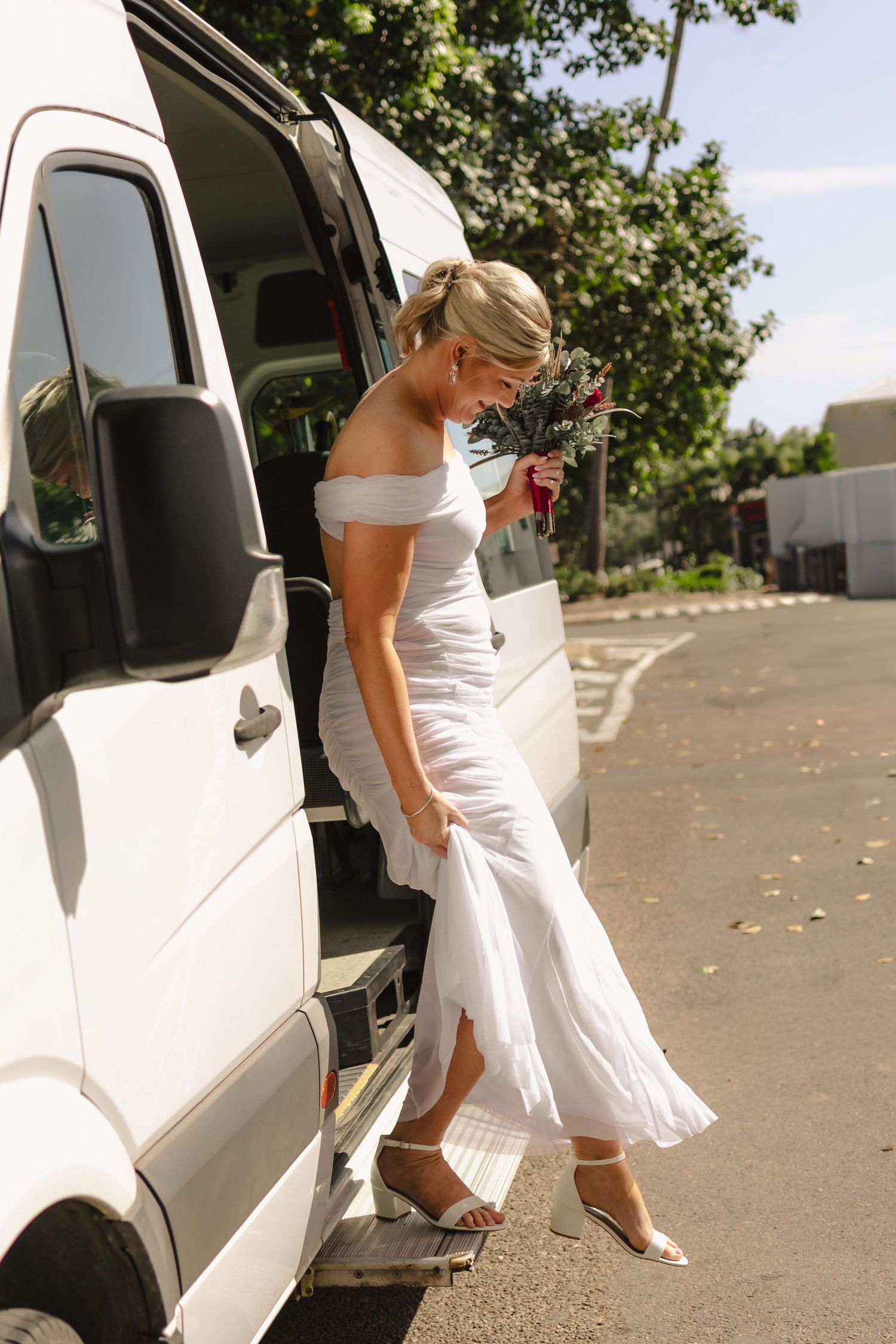 Person in white dress stepping out of a white vehicle at an outdoor venue.