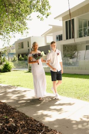 Wedding party walking along a paved pathway outside a white building.