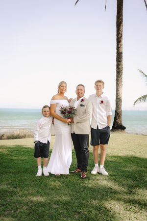 A family poses together on a tropical beach with palm trees in the background.