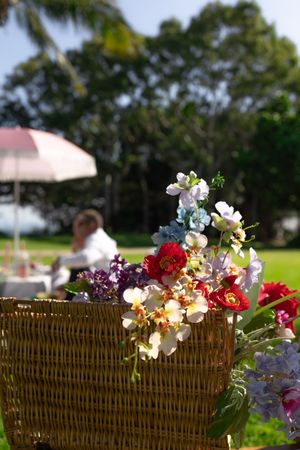 A colorful floral arrangement in a wicker basket at an outdoor wedding.