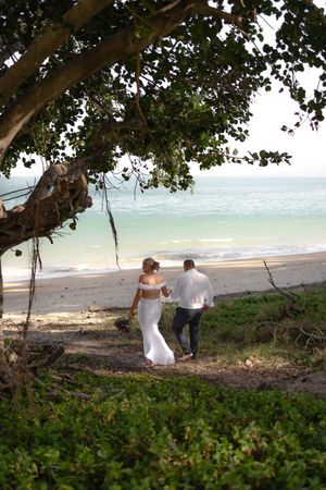 Couple sitting together on a tropical beach under trees with ocean view in the background.