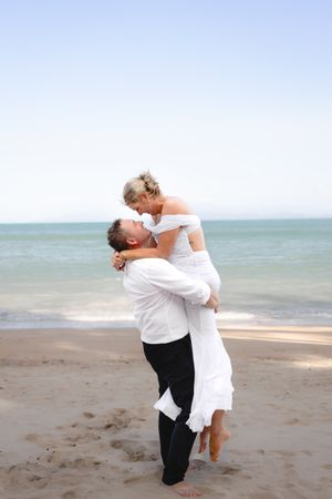 Playful couple embracing on a beach with turquoise ocean waters in the background.