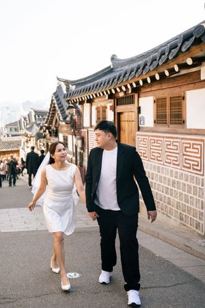 A couple walks along traditional Korean architecture walls in a playful photoshoot sequence.