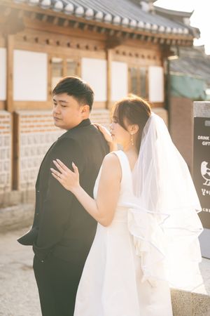 Couple embracing near traditional Korean architecture in soft sunlight.