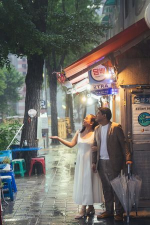 People walking with umbrellas on a rainy day along a storefront-lined street.