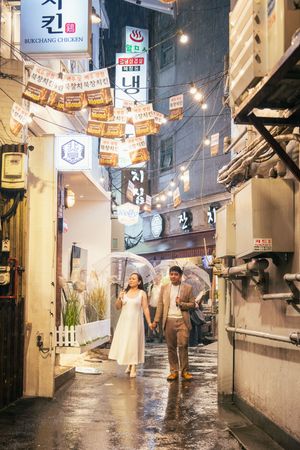 Rainy evening street scene in Korea with illuminated signs and storefronts reflecting on wet pavement.