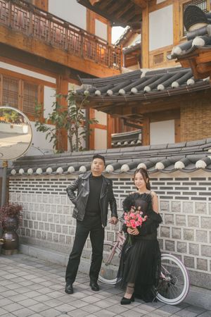 People in formal black attire pose along traditional Korean stone walls and wooden architecture.