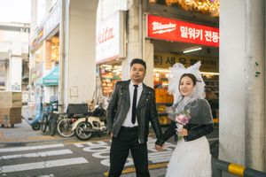 A couple in wedding attire poses together in front of an urban street with storefronts and signage in Korea.