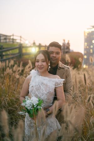 Romantic wedding couple embraces in golden field at sunset with tall grass swaying in the breeze.